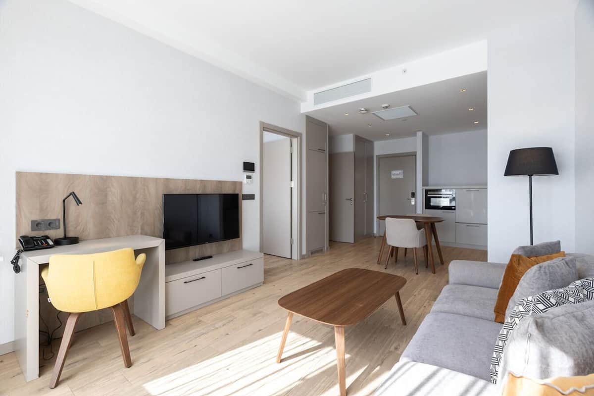 Un salón moderno con televisor, una butaca amarilla, una mesa de centro de madera y un sofá gris.