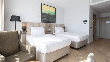 Habitación de hotel con dos camas, un sofá, una lámpara y un cuadro de un paisaje urbano en la pared.