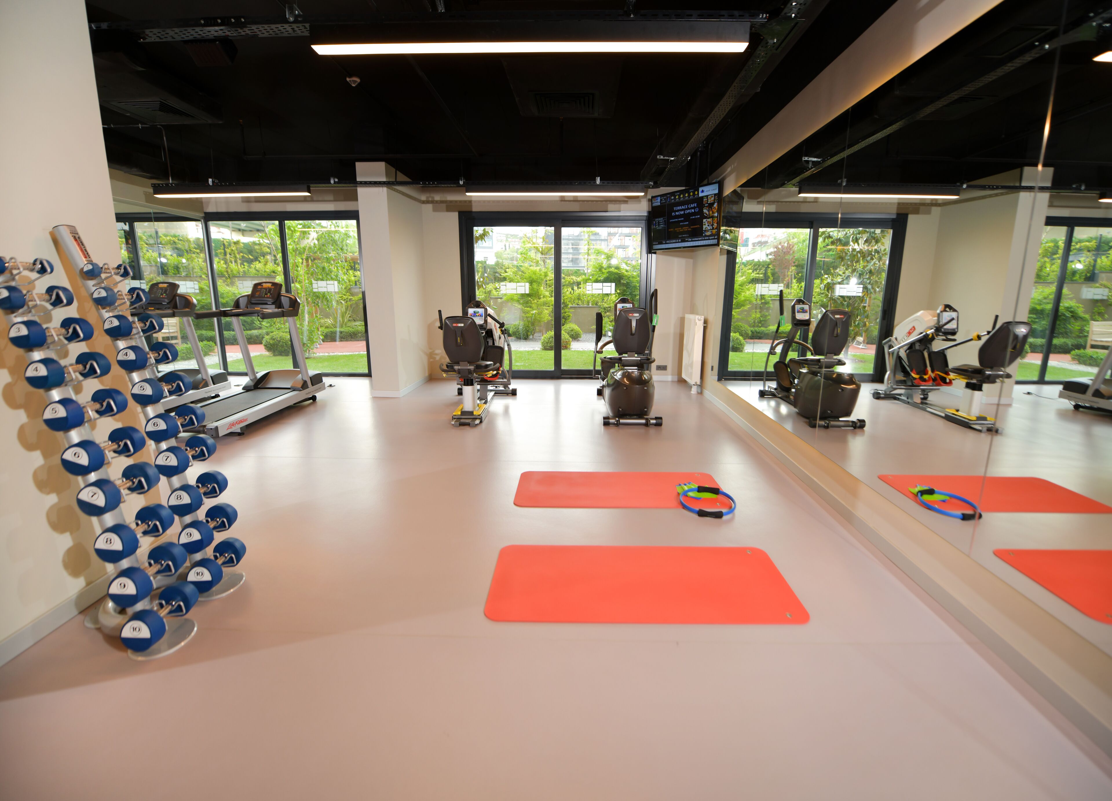 Ein Fitnessstudio mit Trainingsgeräten, Laufbändern und roten Matten.