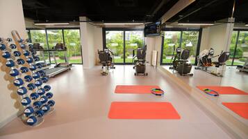 Ein Fitnessstudio mit Trainingsgeräten, Laufbändern und roten Matten.