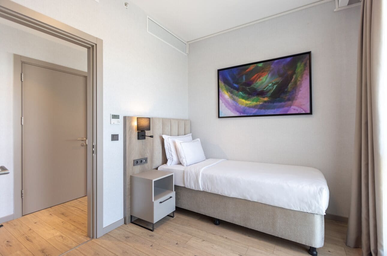 A bedroom with a bed, bedside table, and a wall-mounted abstract painting.