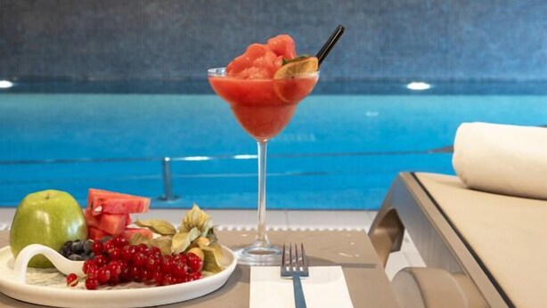 A dining table with a fruit platter, a glass of red drink, and a view of a swimming pool. -  Antwell Suites (Istanbul)