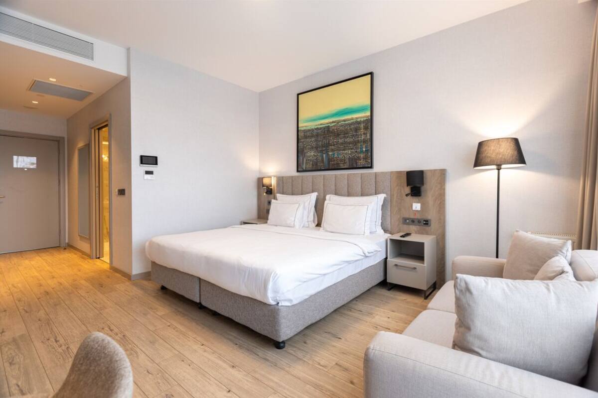 Habitación de hotel moderna con una cama grande, una mesita de noche, una lámpara y un cuadro en la pared.
