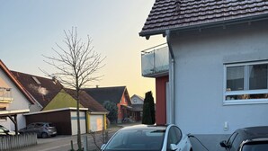 A white Tesla parked in a residential driveway with a clear road and a 'P' parking sign.