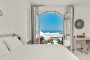 A modern hotel room with a large bed, a view of the sea, and a pool. - Oyster Luxury Suites (Santorini)