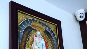 A framed artwork of a seated figure on a throne, with a camera mounted on the wall to the right. - Sai Lodge (Tiruchirappalli)