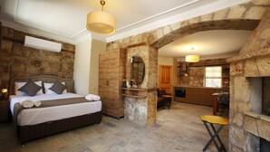 A bedroom with a stone wall, a wooden bed, a small table, and a kitchen area with a stone fireplace. - Castle Inn Boutique Hotel (Antalya)