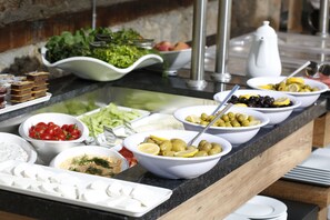 Ein reichhaltiges Buffet mit verschiedenen Speisen, darunter Oliven, Tomaten und Salate.