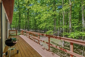 Une terrasse en bois équipée d’un barbecue, entourée d’une zone boisée.
