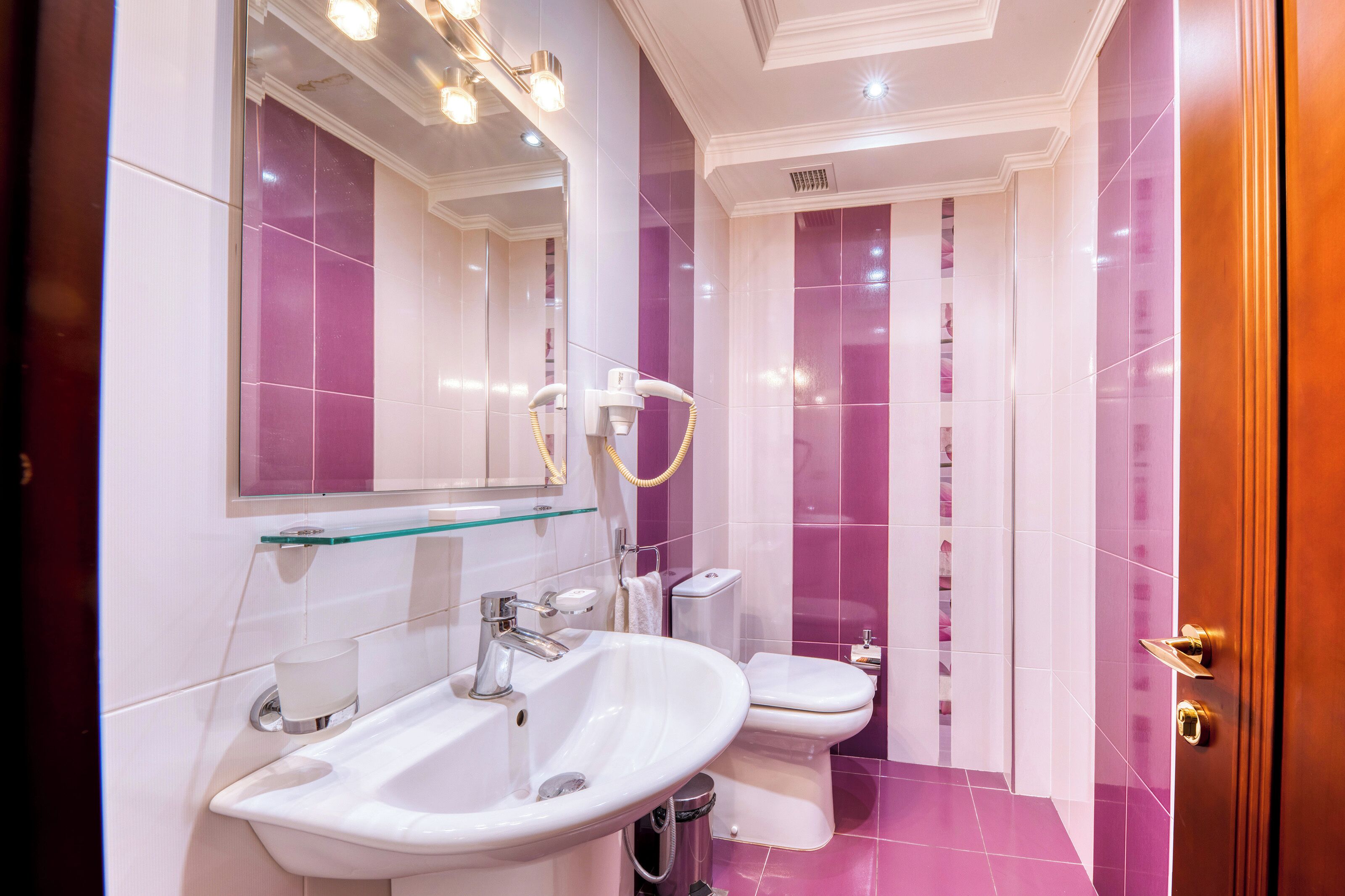 Une salle de bain moderne avec un lavabo blanc, un miroir et des toilettes, ainsi que des carreaux violets.