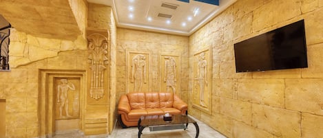 A room with a stone wall, a leather sofa, a glass coffee table, and a flat-screen TV mounted on the wall.