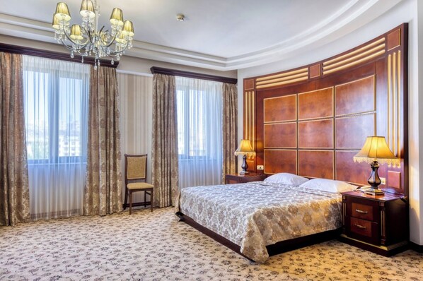 Een ruime hotelkamer met een groot bed, een stoel, een kroonluchter en een groot raam met gordijnen.
