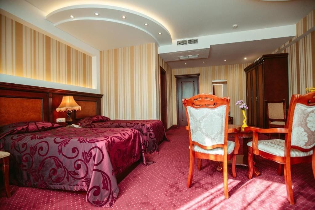 Een hotelkamer met een groot bed, twee stoelen, een tafeltje en een spiegel.