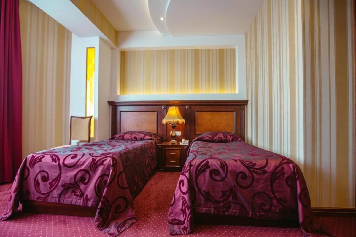 A hotel room with two beds, a nightstand with a lamp, and striped wallpaper.