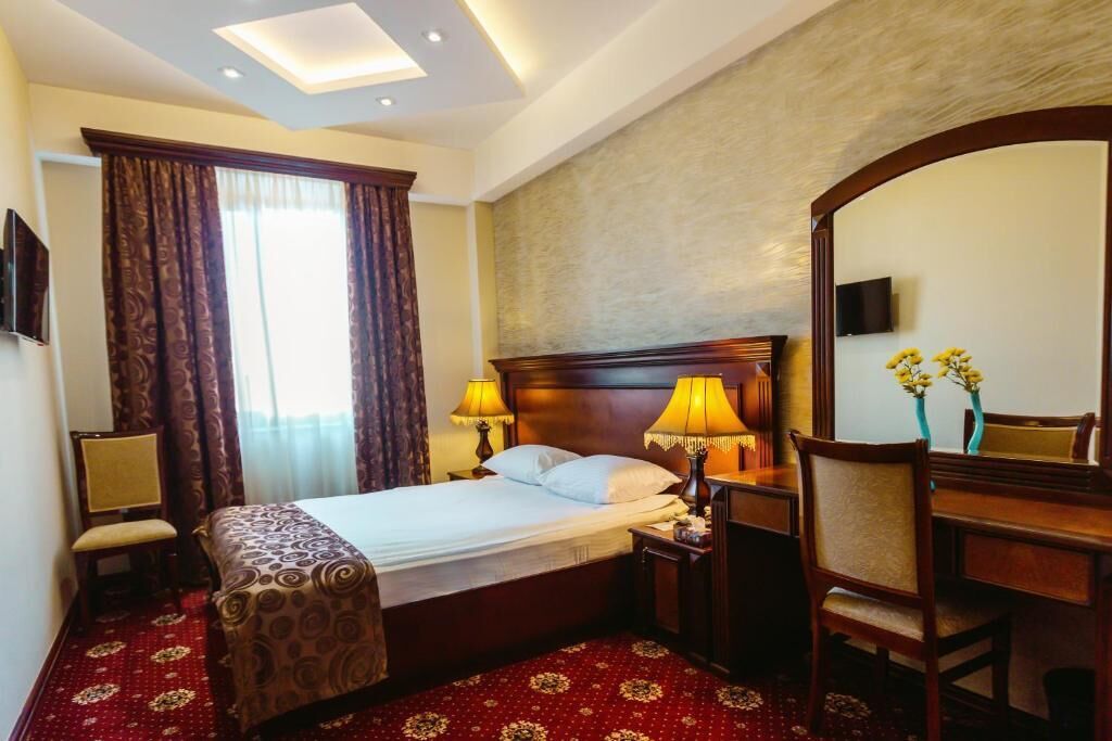 Habitación de hotel con una cama grande, dos lámparas de noche, un cabecero de madera, un escritorio con una silla, un televisor montado en la pared y un espejo grande.