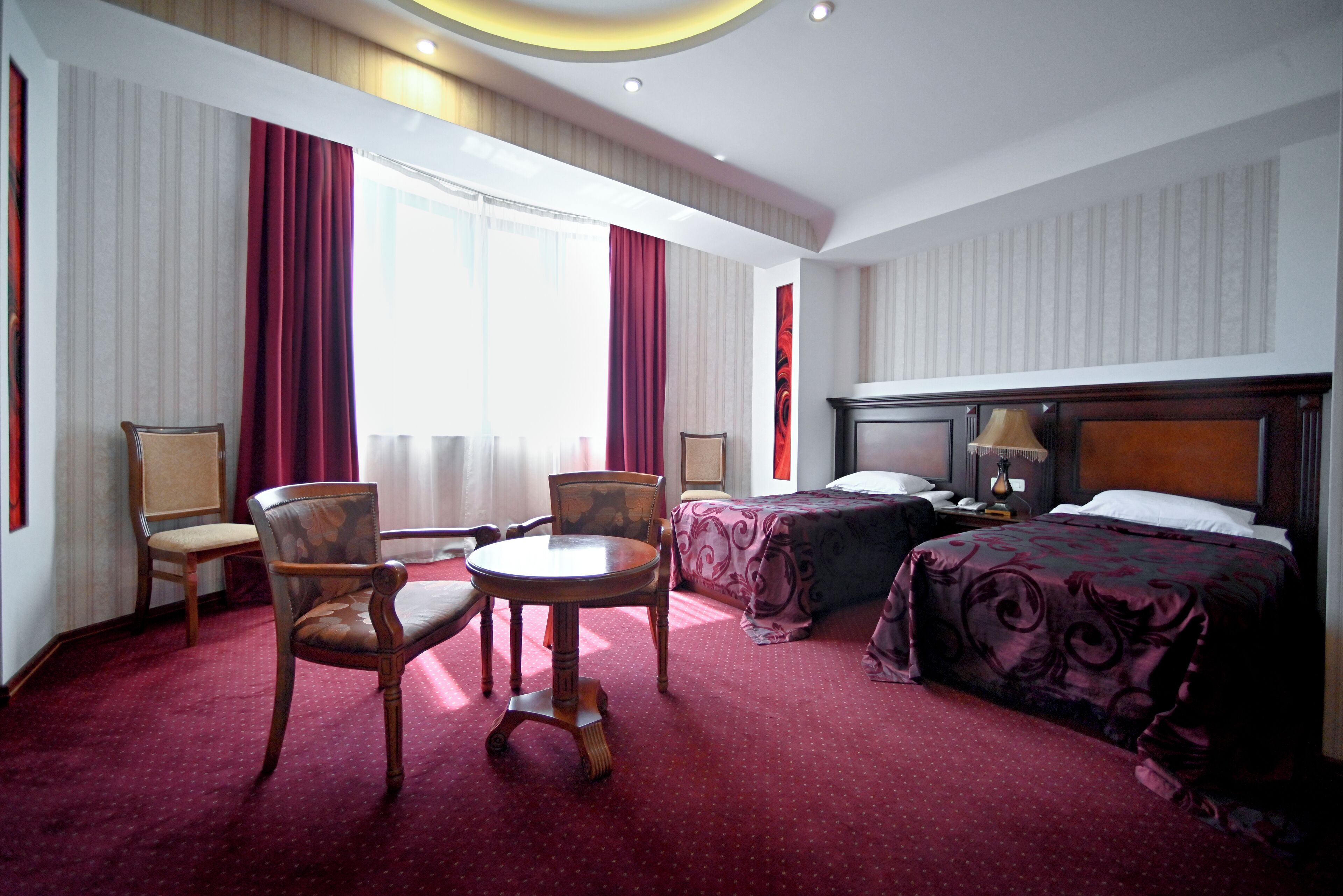 Een hotelkamer met een bed, twee stoelen, een kleine tafel en een nachtkastje met een lamp.