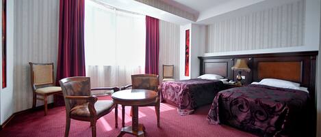 Una habitación de hotel con una cama, dos sillas, una mesita y una mesita de noche con una lámpara.