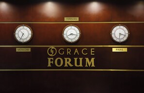 Drie klokken met de namen van steden: Moskou, Jerevan en Parijs, op een muur met de tekst 'GRACE FORUM'.