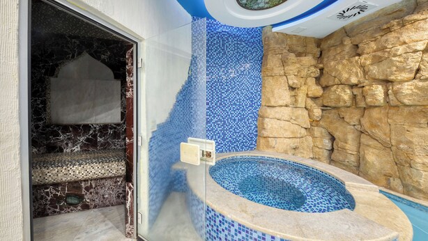 Un baño con pared de mosaicos, pared de piedra y bañera con detalles de mosaicos.