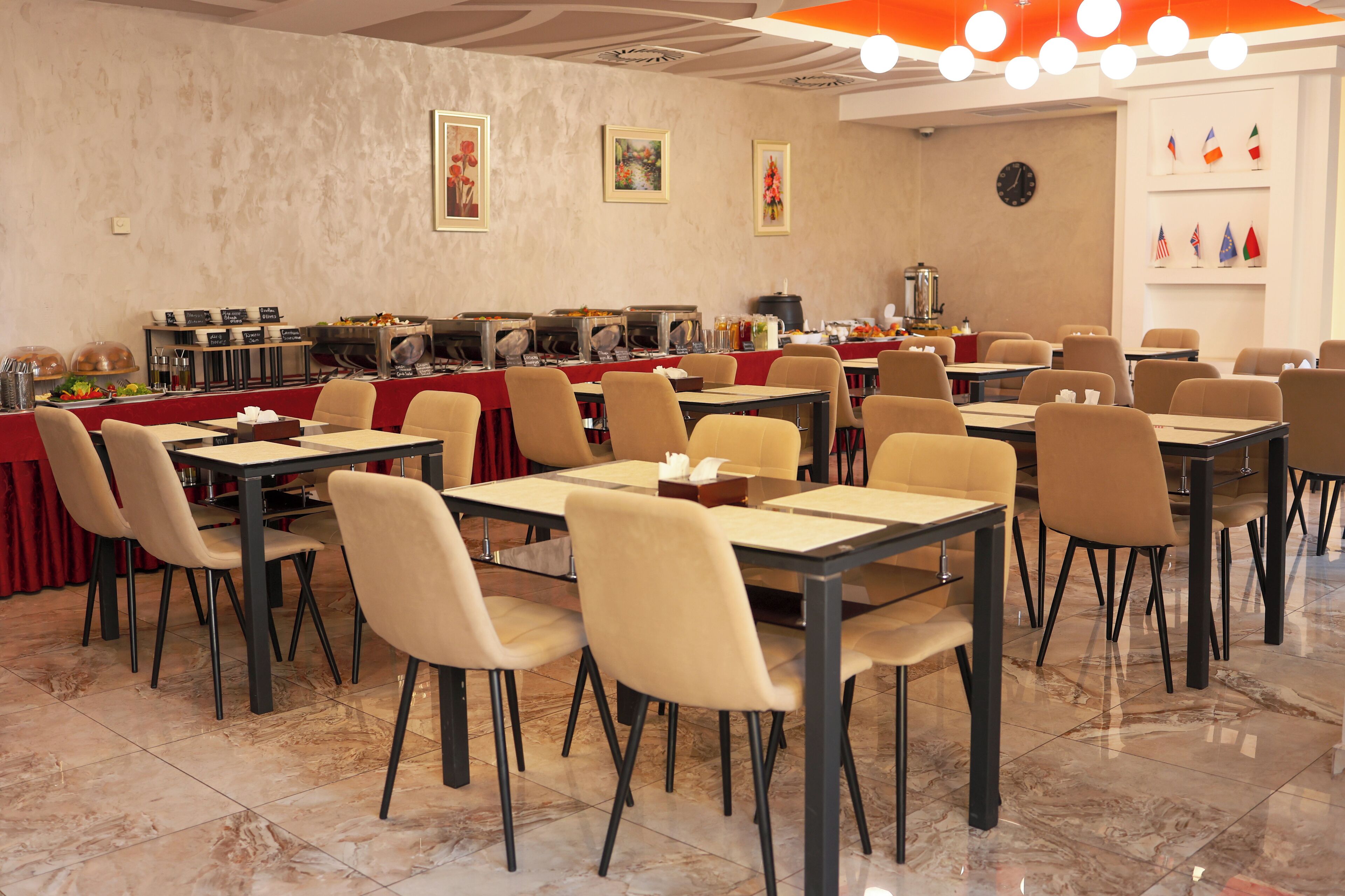 A dining area with multiple tables and chairs, a buffet line with various food items, and a clock on the wall.