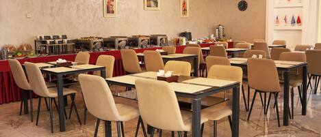 A dining area with multiple tables and chairs, a buffet line with various food items, and a clock on the wall.
