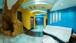 Un vestíbulo con un sofá blanco, una gran estructura rocosa y una pared azul con obras de arte enmarcadas.
