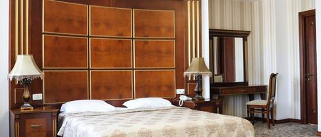 A hotel room with a large bed, a wooden headboard, a desk with a chair, a mirror, and a lamp.