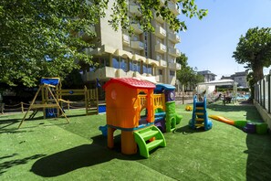 Un parque infantil con diversas estructuras de juego, rodeado por un edificio con balcones.