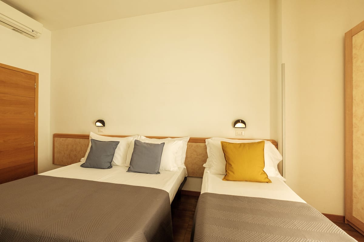 A hotel room with two beds, each with a pillow and a bedside lamp.