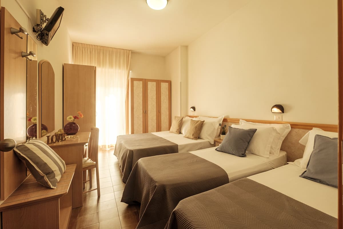 A hotel room with two beds, a desk, a chair, a mirror, and a wardrobe.
