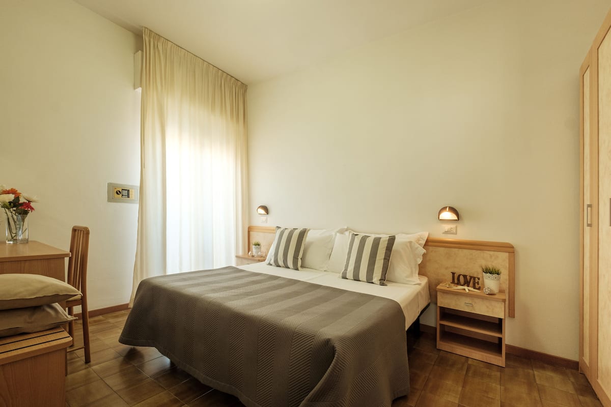 A neatly arranged hotel room with a bed, bedside tables, a chair, and a small desk.