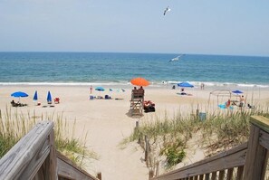 A beach with umbrellas, beach chairs, and a lifeguard stand. - Seawalk 3-Bed Condo with Ocean Views (Kill Devil Hills)
