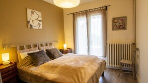 A bedroom with a large bed, bedside lamps, a radiator, and a window with curtains. - Renovated house with WiFi and terrace in Trélissac (Trélissac)