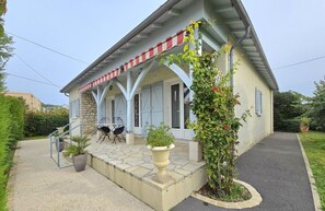 A two-story building with a stone facade, a covered porch with red and white striped awnings, and a small garden area with potted plants and a climbing vine. - Renovated house with WiFi and terrace in Trélissac (Trélissac)