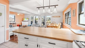 A modern kitchen with a wooden countertop, white cabinetry, and a dining area with a wooden table and chairs. - 6129 Lady Jane * Semi-Oceanfront * Hot Tub (Nags Head)
