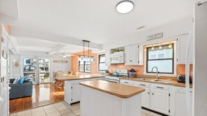 A modern kitchen with white cabinetry, a central island, and a dining area with a blue sofa. - 6129 Lady Jane * Semi-Oceanfront * Hot Tub (Nags Head)