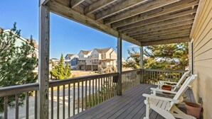 A wooden deck with a covered porch, white rocking chairs, and a view of a residential area with houses. - 6154 Little Sushi * 2 Min Walk to Beach (Nags Head)