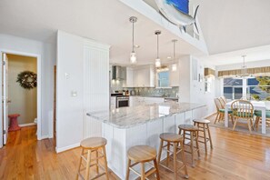 A spacious kitchen with a large island, wooden stools, and pendant lighting.