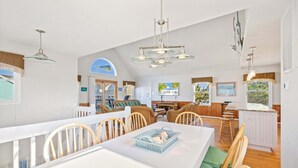 A spacious kitchen with a dining area, wooden chairs, a white table, and a large window with a view. - 6154 Little Sushi * 2 Min Walk to Beach (Nags Head)