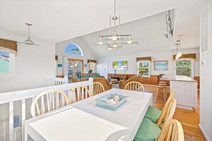A spacious kitchen with a dining area, wooden chairs, a white table, and a large window with a view.