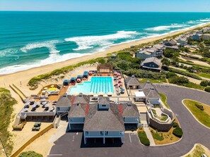 An aerial view of a coastal resort with a swimming pool, beach access, and residential buildings.