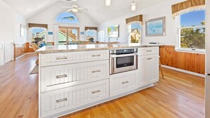 A spacious kitchen with a large island, wooden flooring, and a view of the outside. - 6154 Little Sushi * 2 Min Walk to Beach (Nags Head)