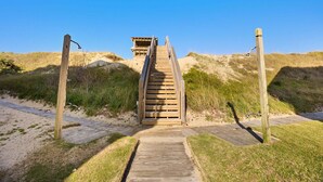 A wooden boardwalk leading to a beach house with a sandy beach and dunes in the background. - Family Oceanfront Escape | 3BR, Pool & Beach Access (Nags Head)