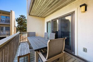 A balcony with a wooden table and chairs, a sliding glass door, and a view of a neighboring building.