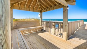 A wooden deck with a covered seating area overlooking a beach. - Family Oceanfront Escape | 3BR, Pool & Beach Access (Nags Head)