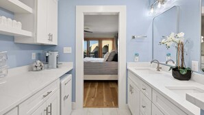 A modern bathroom with white fixtures, a large mirror, and a potted orchid. - Family Oceanfront Escape | 3BR, Pool & Beach Access (Nags Head)