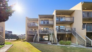 A multi-story residential building with balconies, a central staircase, and a well-maintained lawn. - Family Oceanfront Escape | 3BR, Pool & Beach Access (Nags Head)