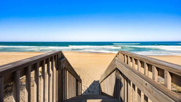 A wooden boardwalk leading to a sandy beach with ocean waves. - Family Oceanfront Escape | 3BR, Pool & Beach Access (Nags Head)