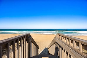 A wooden boardwalk leading to a sandy beach with ocean waves.