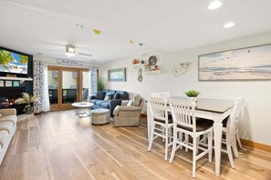 A cozy living area with a fireplace, a dining table with chairs, a sofa, and a TV screen displaying a beach scene.